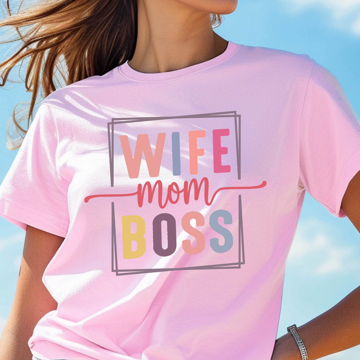 May include: A light pink t-shirt with the words "WIFE mom BOSS" in colorful block letters. The text is inside a gray rectangular frame with a red line underneath the word "WIFE" and above the word "BOSS".