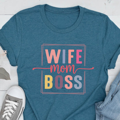 May include: Teal-colored t-shirt with the words "WIFE mom BOSS" in a colorful, rectangular design. The text is in various colors, including pink, orange, yellow, and blue. A gray canvas shoe is visible in the lower left corner.