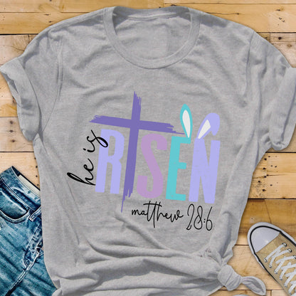 May include: A gray t-shirt with a purple, blue, and pink graphic that says "He is Risen" with a cross and bunny ears. The text "Matthew 28:6" is below the graphic.