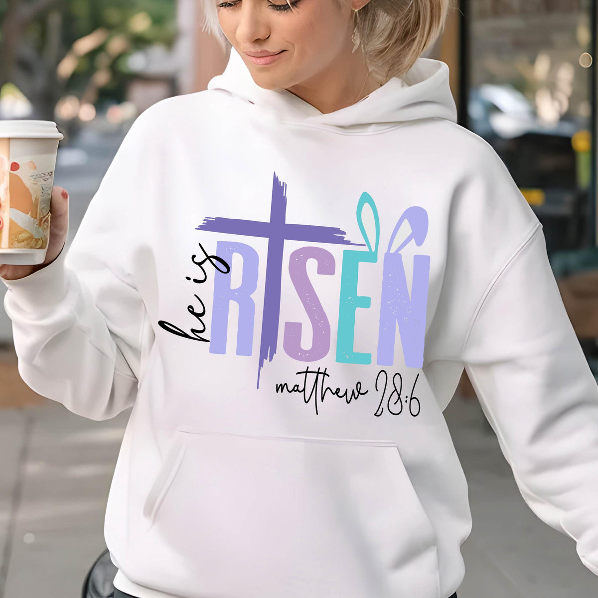 May include: White hoodie with a purple, blue, and pink graphic that says "He is Risen" with a cross and bunny ears. The text "Matthew 28:6" is below the graphic.