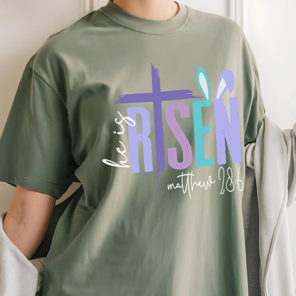 May include: Green t-shirt with a colorful graphic that says "He is Risen" with a cross and bunny ears. The text "Matthew 28:6" is below the graphic.