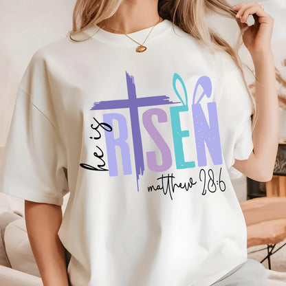 May include: White t-shirt with a purple, pink, and blue graphic that says "He is Risen" with a cross and bunny ears. The text "Matthew 28:6" is below the graphic.