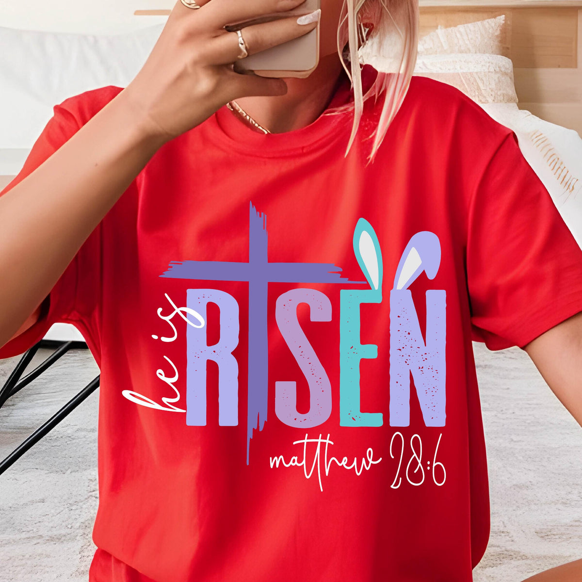May include: Red t-shirt with a purple, blue, and green graphic that says "He is Risen" with a cross and bunny ears. The text "Matthew 28:6" is below the graphic.