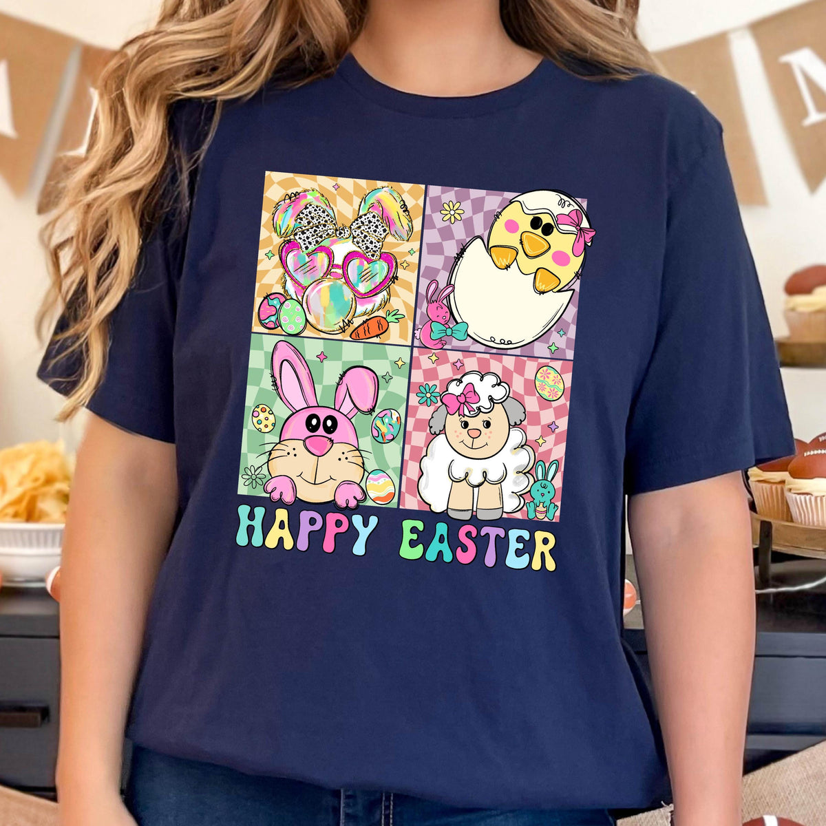May include: Navy blue t-shirt with a colorful graphic featuring Easter-themed characters: a bunny, chick, and lamb. The design includes the words "HAPPY EASTER" in a rainbow font. The shirt has a classic crew neck.