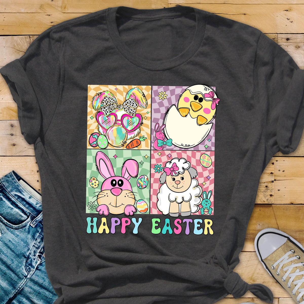 May include: Dark gray t-shirt featuring a colorful Easter-themed graphic. The design includes four squares with cartoon images of a bunny, chick, lamb, and the words "HAPPY EASTER" in pastel colors. The shirt is made of a soft material.