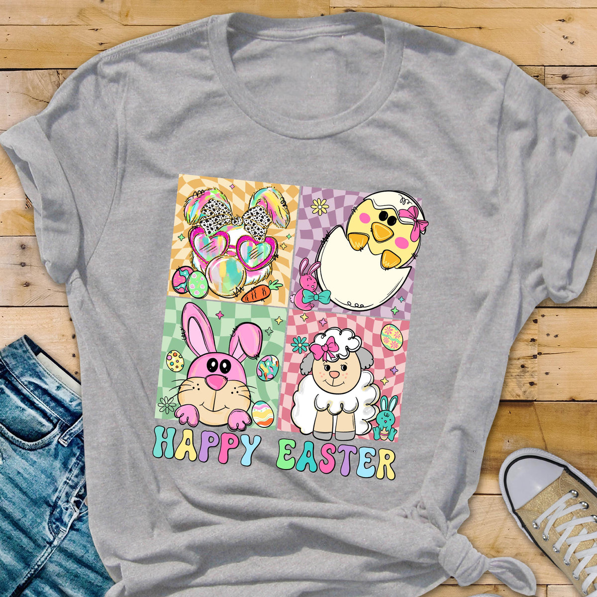 May include: A gray t-shirt featuring a colorful Easter-themed graphic. The design includes a bunny with sunglasses, a chick hatching from an egg, a pink bunny, and a sheep. The words "HAPPY EASTER" are written in colorful letters.