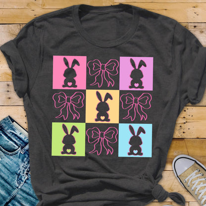 May include: A dark gray t-shirt with a colorful design of nine squares. Each square features a silhouette of a bunny with a bow. The squares are in alternating colors of pink, blue, green, and yellow.