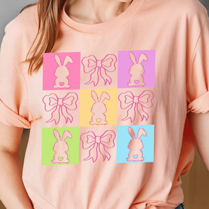 May include: A pink t-shirt with a colorful design of bunnies and bows. The design is made up of nine squares, each with a different color and a different bunny or bow design.