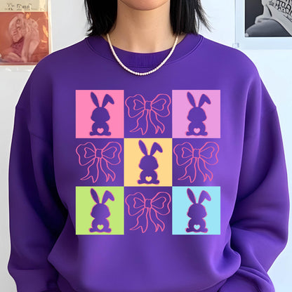 May include: Purple sweatshirt with a graphic of nine colorful squares featuring pink, yellow, blue, and green bunnies with pink bows. Each bunny has a small pink heart on its chest.