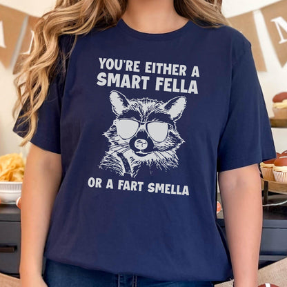 May include: A navy blue t-shirt with a white graphic of a raccoon wearing sunglasses and the text "You're either a smart fella or a fart smella".