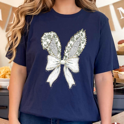 May include: A navy blue t-shirt with a white bow and green floral bunny ears design.
