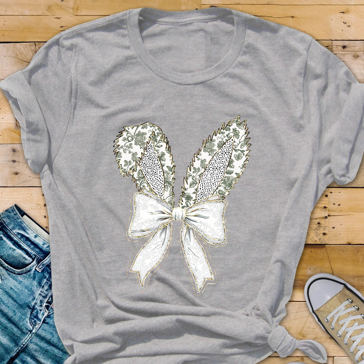May include: A gray t-shirt with a white bow and two green and gold bunny ears. The bow has a gold glitter design.