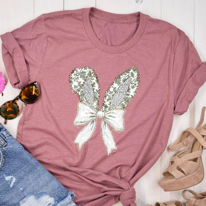 May include: A mauve t-shirt with a white bow and green floral bunny ears graphic.