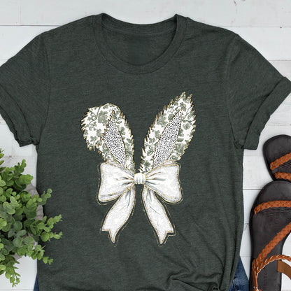 May include: A dark green t-shirt with a white bow and bunny ears design. The bow and ears are decorated with a floral pattern and gold glitter.