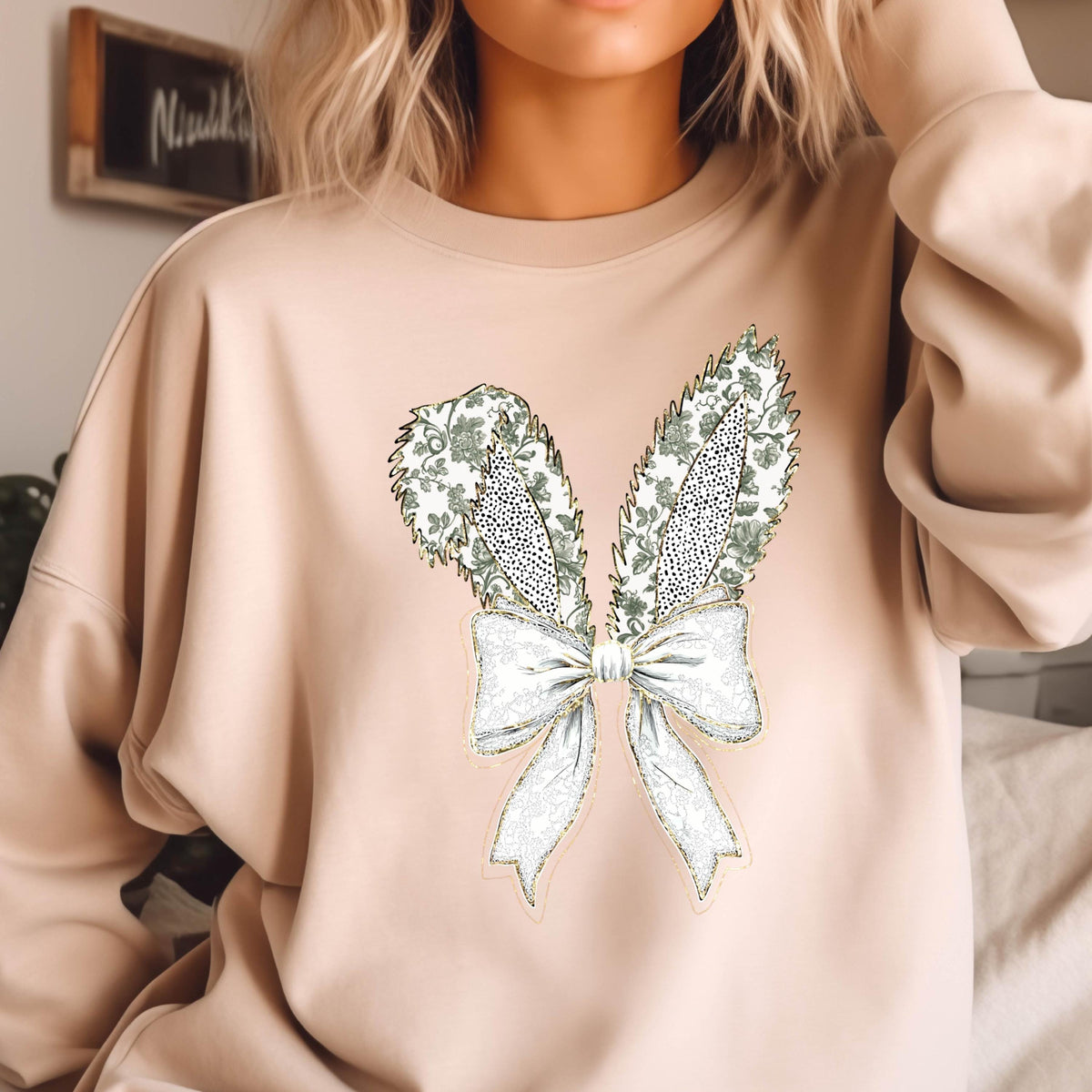 May include: A beige sweatshirt with a white and green bunny rabbit design. The bunny has a large bow with a floral pattern.