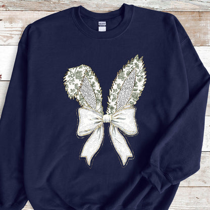 May include: A navy blue sweatshirt with a white and gold bow and bunny ears design. The bow is tied with a large, decorative knot.