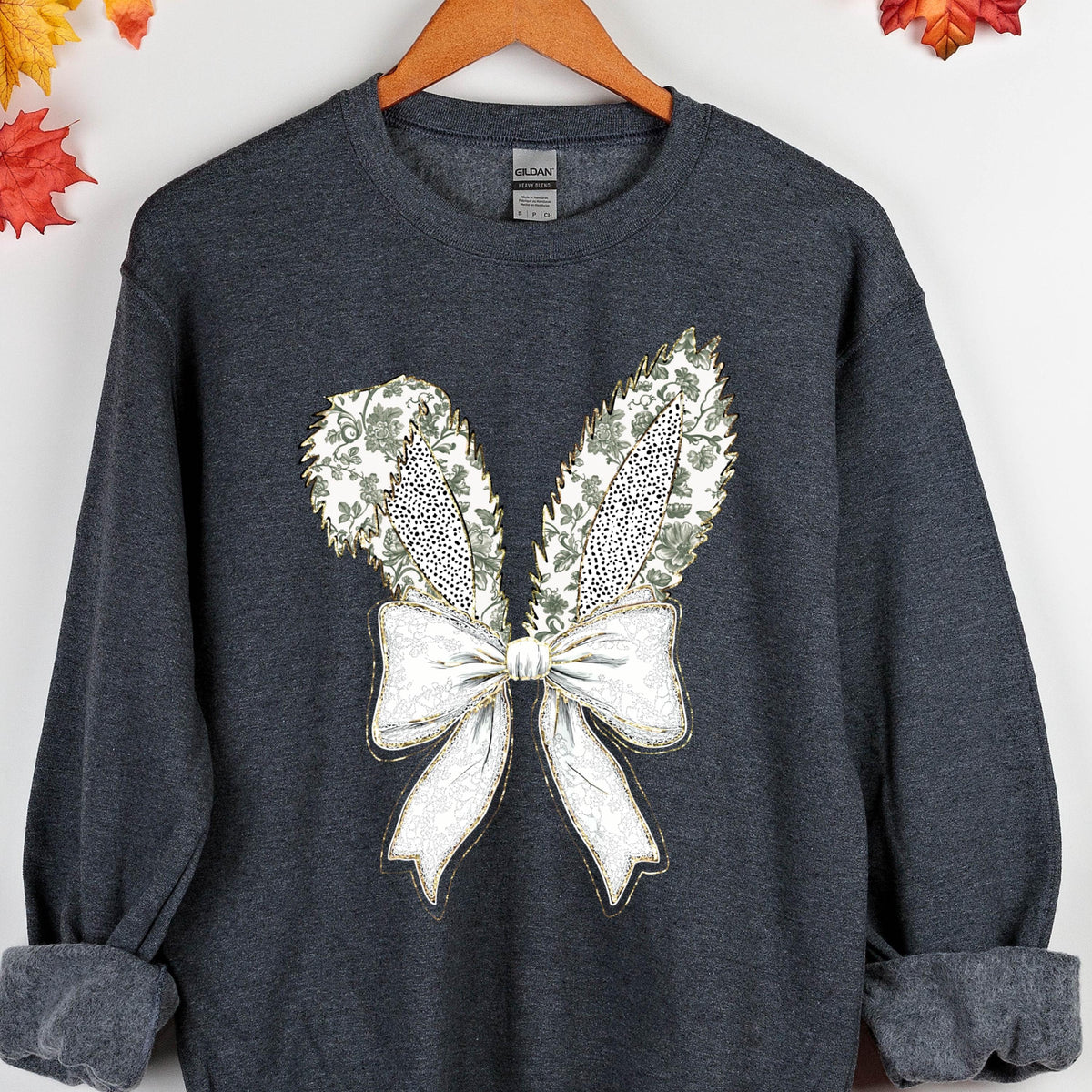 May include: A dark gray sweatshirt with a white and gold embroidered design of a bow with bunny ears. The bow has a floral pattern.