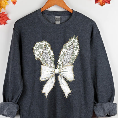 May include: A dark gray sweatshirt with a white and gold embroidered design of a bow with bunny ears. The bow has a floral pattern.