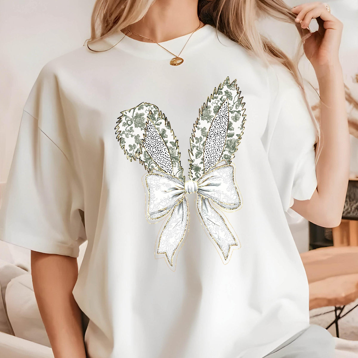 May include: White t-shirt with a gold and green bow design. The bow is made of a floral pattern and has a gold outline.