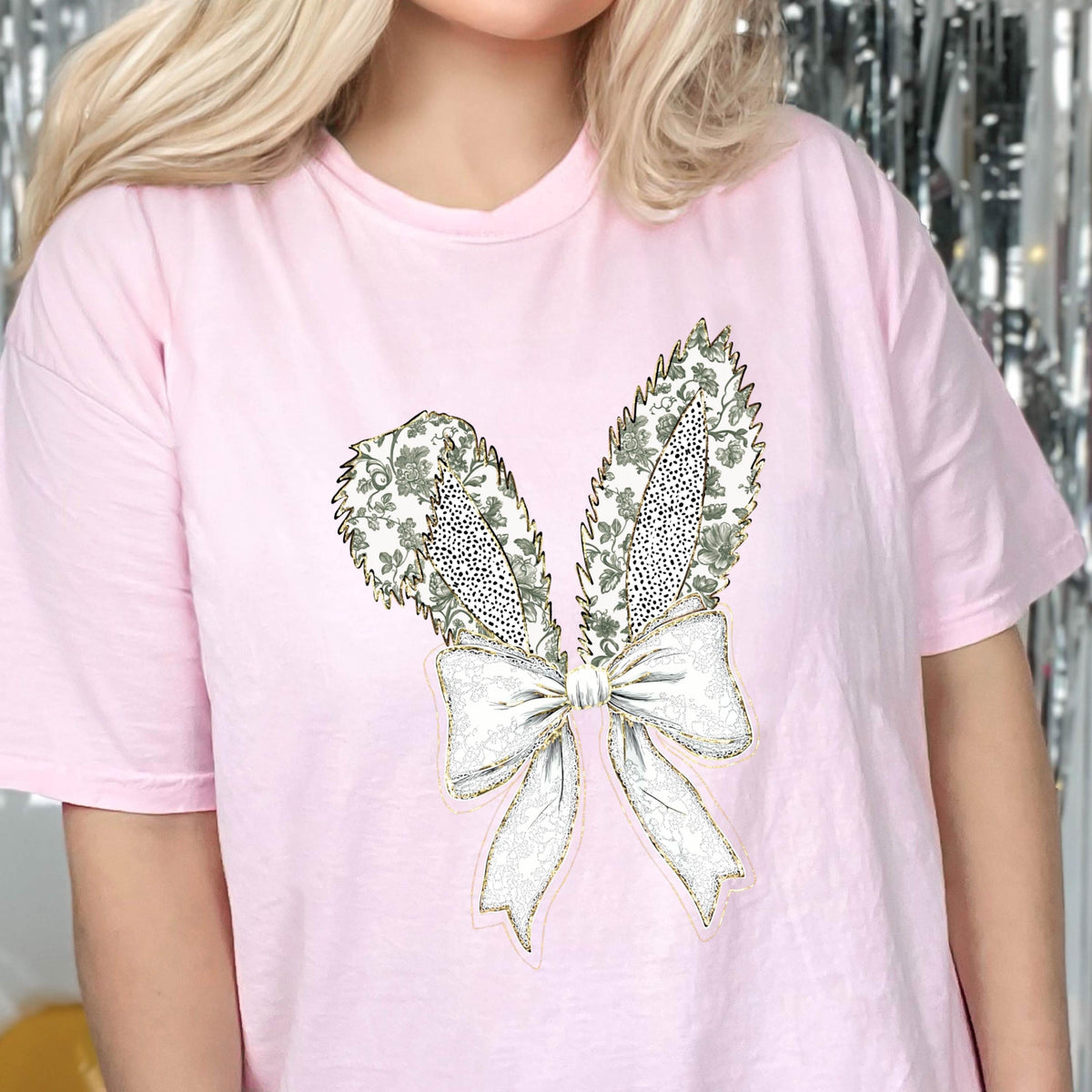 May include: A pink t-shirt with a white and gold embroidered bunny rabbit design. The bunny has a bow tie and the ears are decorated with a floral pattern.