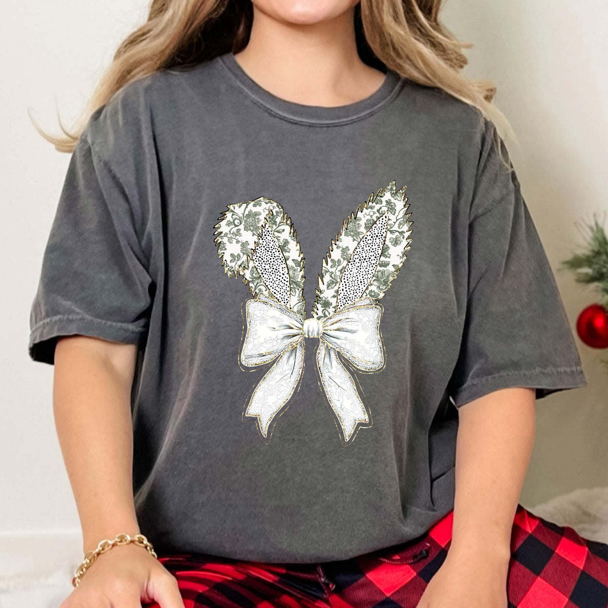 May include: A charcoal gray t-shirt with a white bow and two green and white bunny ears printed on the front.