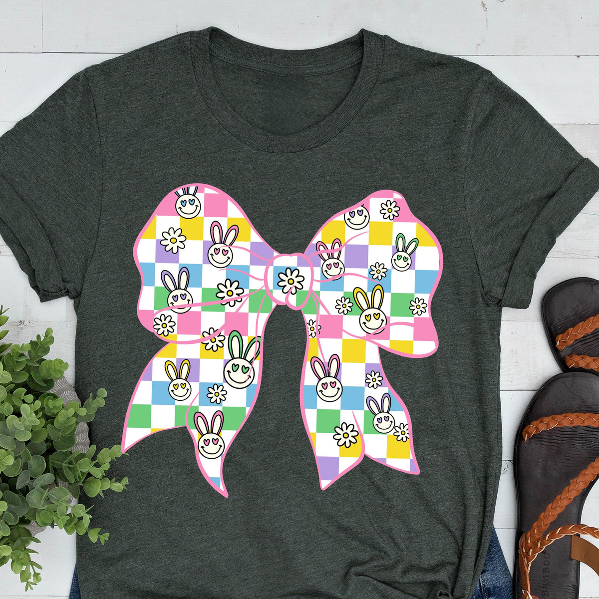 May include: A dark green t-shirt with a pink bow featuring a checkered pattern with colorful bunny faces and white flowers.