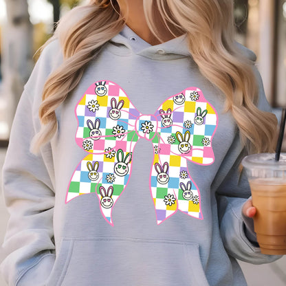 May include: A gray hoodie with a pink bow featuring a checkered pattern of smiling bunnies and flowers. The bow is a large design on the front of the hoodie.