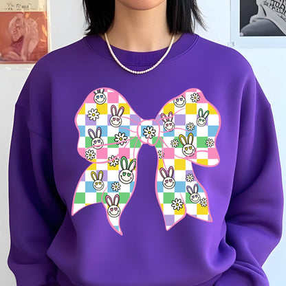 May include: Purple sweatshirt with a large pink bow printed on the front. The bow is checkered with pastel colors and has smiling bunny faces and flowers.