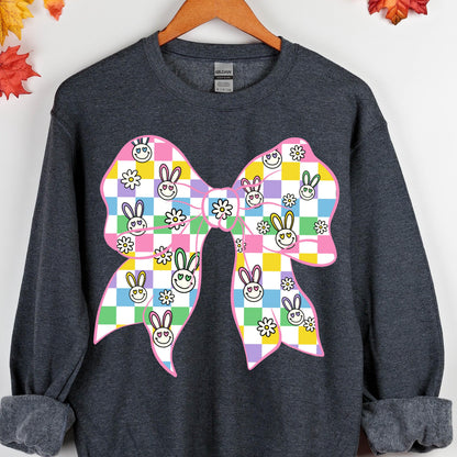 May include: A dark gray sweatshirt with a pink, yellow, green, and blue bow with a checkered pattern. The bow is decorated with bunny faces and flowers.