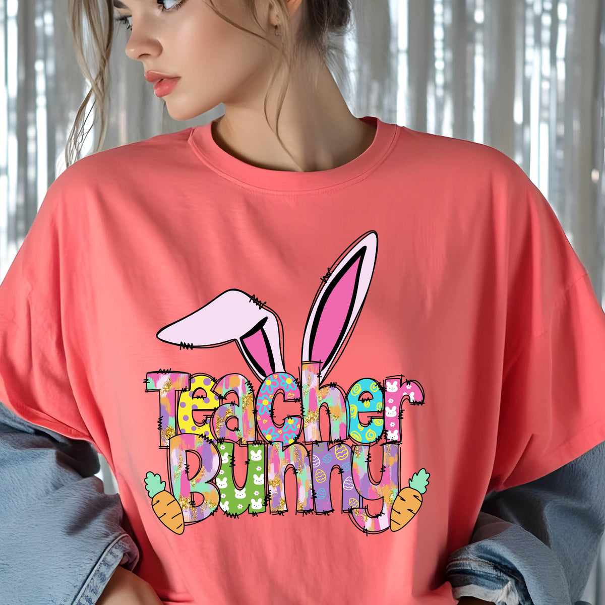 May include: Coral-colored t-shirt featuring a colorful "Teacher Bunny" graphic with bunny ears and carrots. The text is in a playful, multi-colored font. A casual, comfortable tee for Easter or spring.