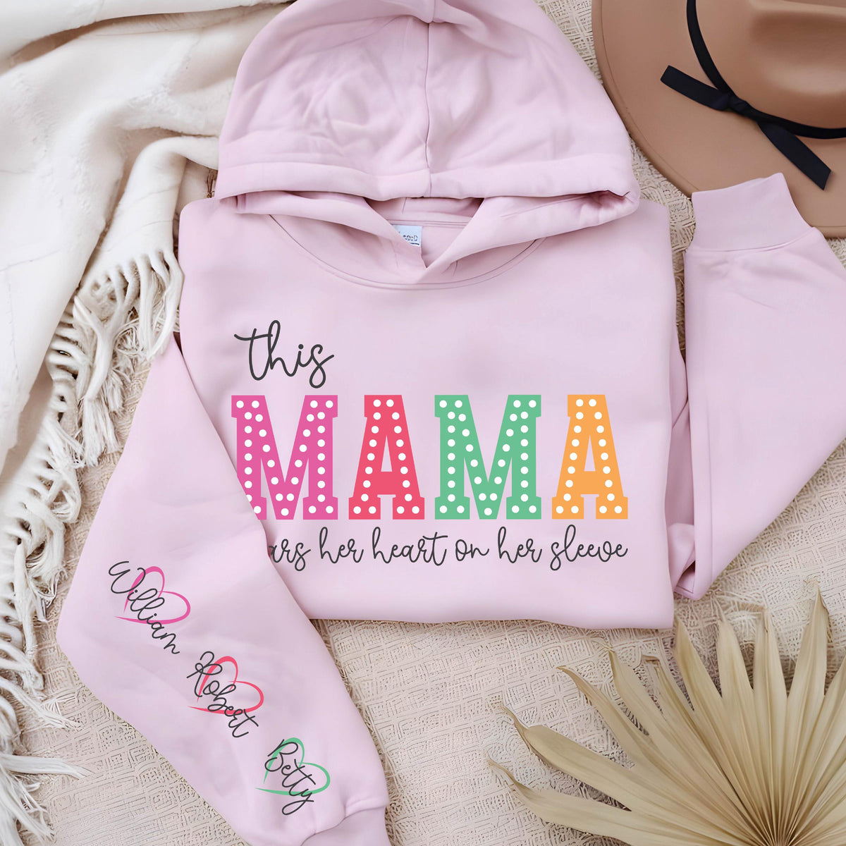 May include: Pink hooded sweatshirt with the text "this MAMA wears her heart on her sleeve" in rainbow letters with white polka dots. The left sleeve has the names "William Robert Betty" written in black with a heart symbol after each name.