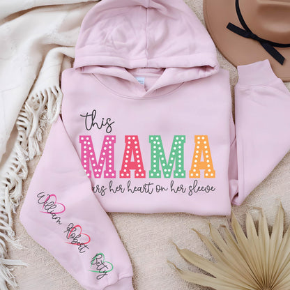 May include: Pink hooded sweatshirt with the text "this MAMA wears her heart on her sleeve" in rainbow letters with white polka dots. The left sleeve has the names "William Robert Betty" written in black with a heart symbol after each name.