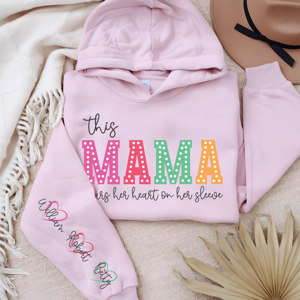 May include: Pink hooded sweatshirt with the text "this MAMA wears her heart on her sleeve" in rainbow letters with white polka dots. The left sleeve has the names "William Robert Betty" written in black with a heart symbol after each name.
