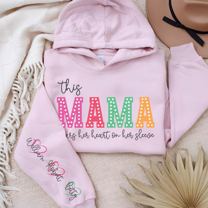 May include: Pink hooded sweatshirt with the text "this MAMA wears her heart on her sleeve" in rainbow letters with white polka dots. The left sleeve has the names "William Robert Betty" written in black with a heart symbol after each name.