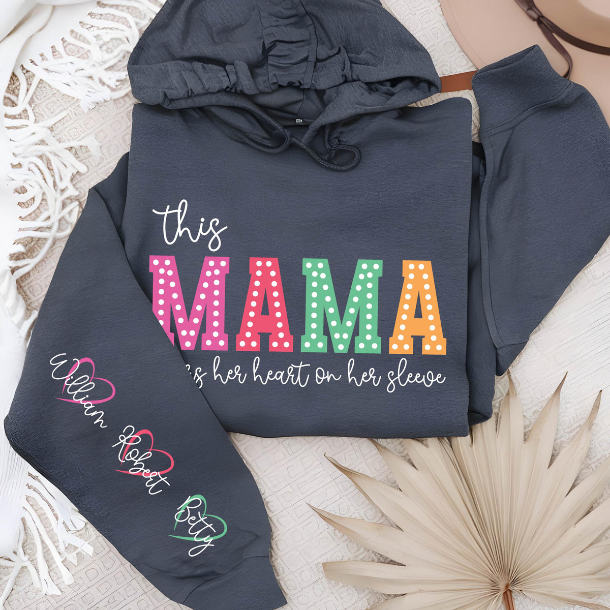 May include: A dark gray hooded sweatshirt with the text "this mama wears her heart on her sleeve" in colorful letters with white polka dots. The sleeve has the names "William, Robert, Betty" written in white with pink hearts.