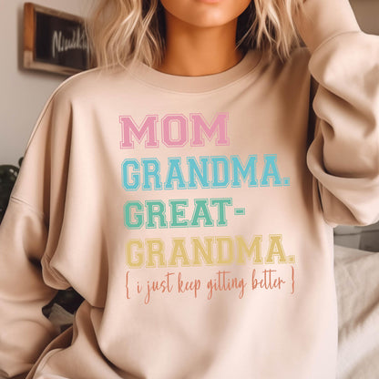 May include: A light beige sweatshirt with the text "MOM GRANDMA. GREAT-GRANDMA. {i just keep getting better}" printed in rainbow colors.