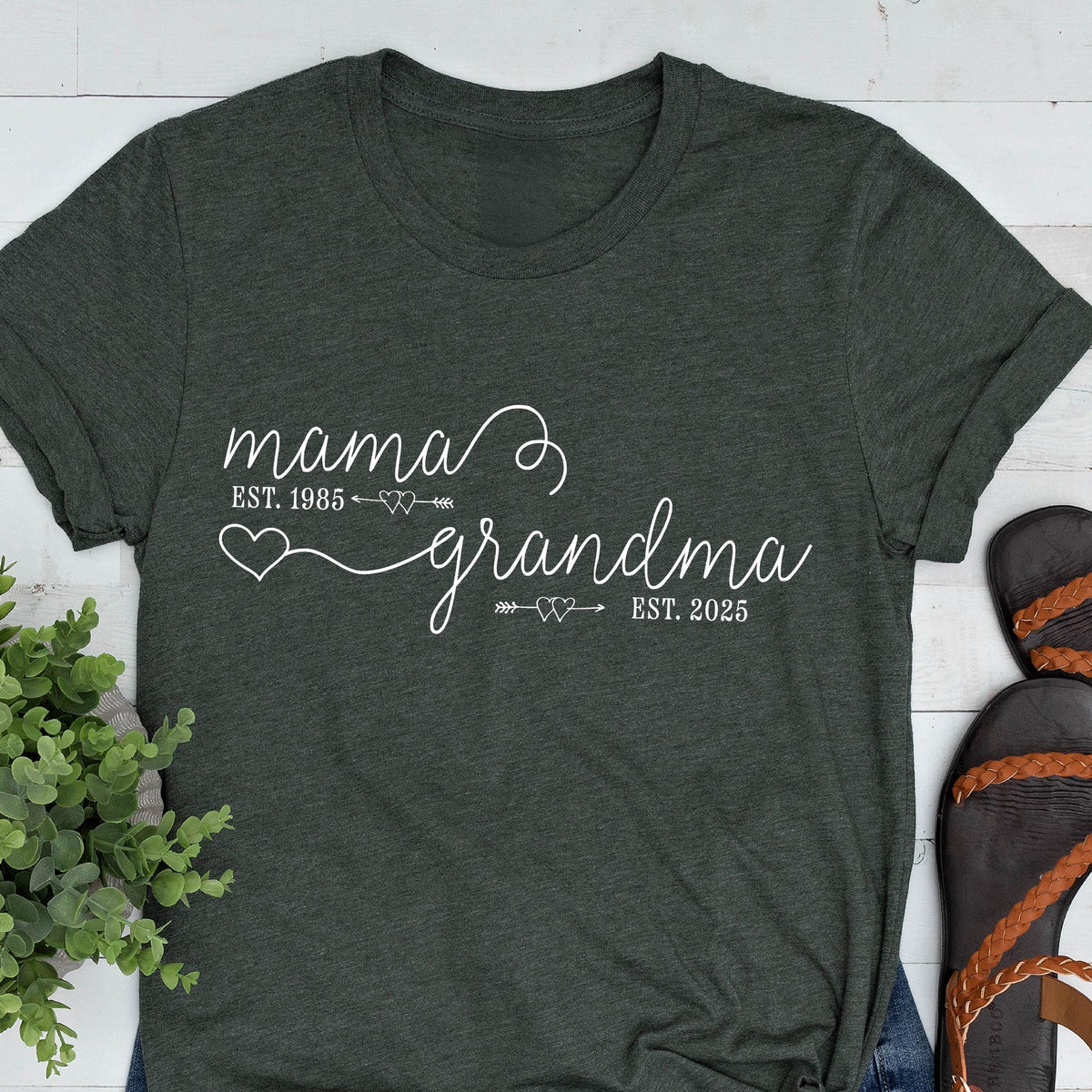 May include: A dark green t-shirt with white text that reads "mama est. 1985" with a heart and arrow, and "grandma est. 2025" with a heart and arrow.