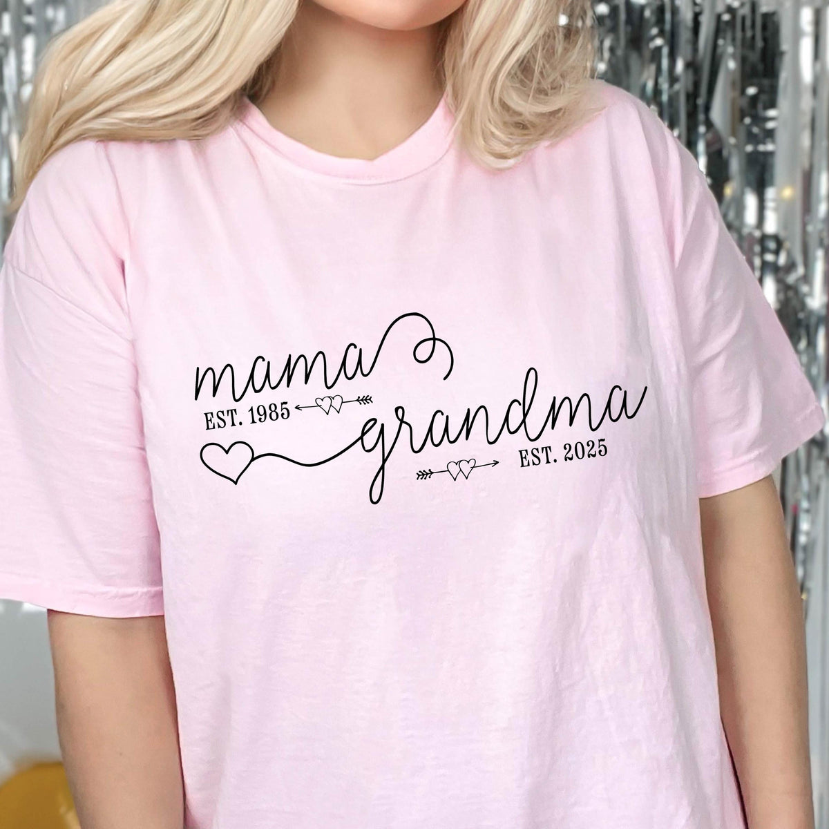May include: Pink t-shirt with the text "mama est. 1985" connected to "grandma est. 2025" with a heart and arrow design.