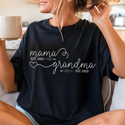 May include: Black t-shirt with white text that reads "mama est. 1985" with a heart and arrow pointing to "grandma est. 2025" with a heart and arrow.