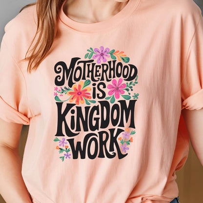 May include: A peach-colored t-shirt with a floral design and the text "Motherhood is Kingdom Work" in black lettering.