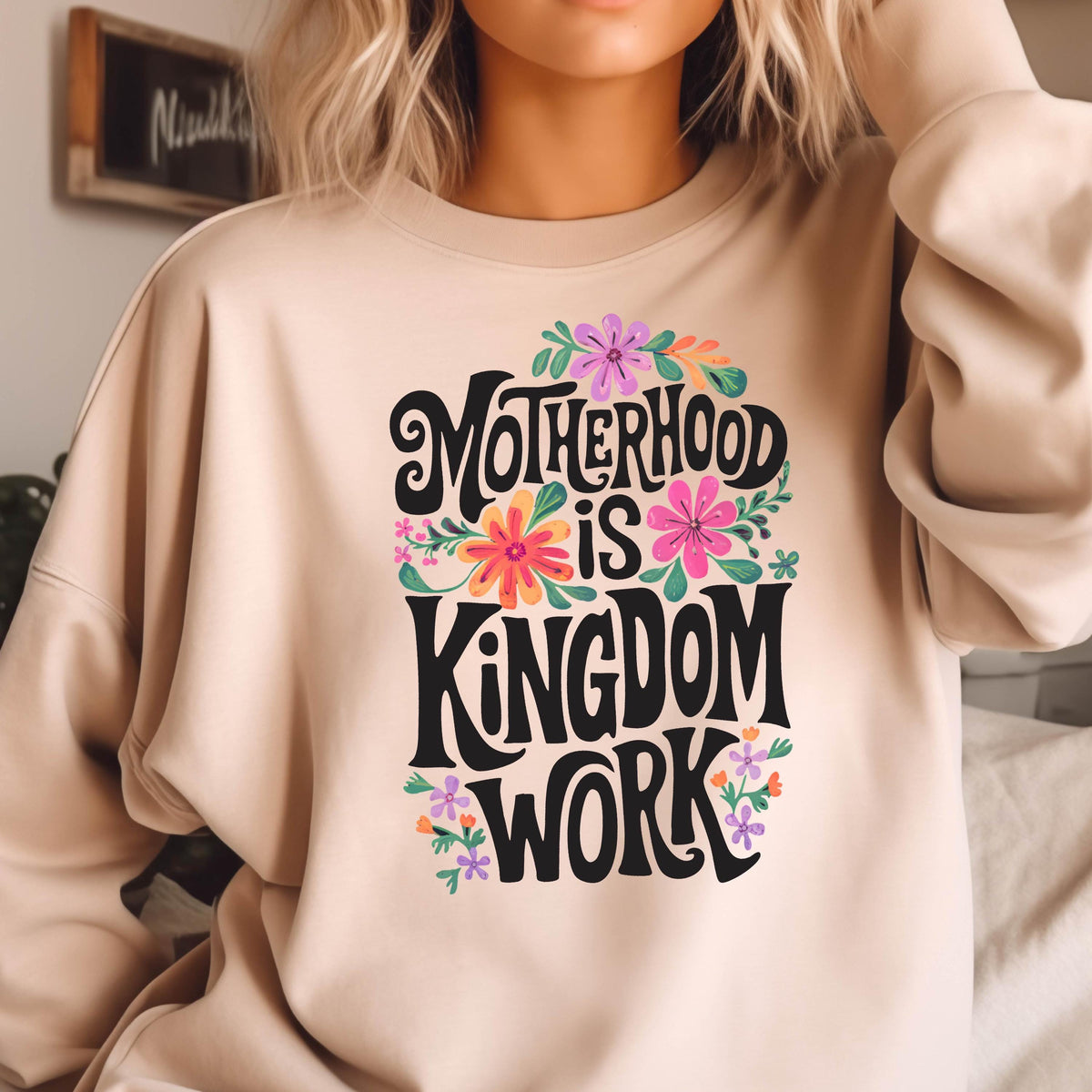 May include: A beige sweatshirt with a floral design and the text "Motherhood is Kingdom Work" in black lettering.