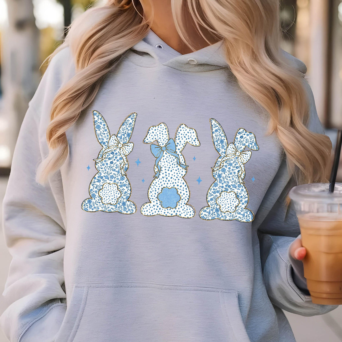 May include: A gray hoodie with a graphic of three blue bunnies with floral patterns and bows. The bunnies are facing away from the viewer.