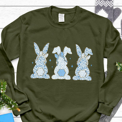 May include: Olive green sweatshirt with a graphic of three blue and white bunny rabbits with blue bows. The bunnies are facing forward and are arranged in a row.
