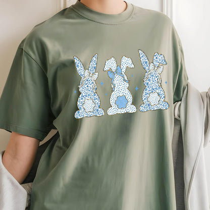 May include: A green t-shirt with a print of three blue bunnies with white polka dots and blue bows. The bunnies are facing forward and have their tails in the air.