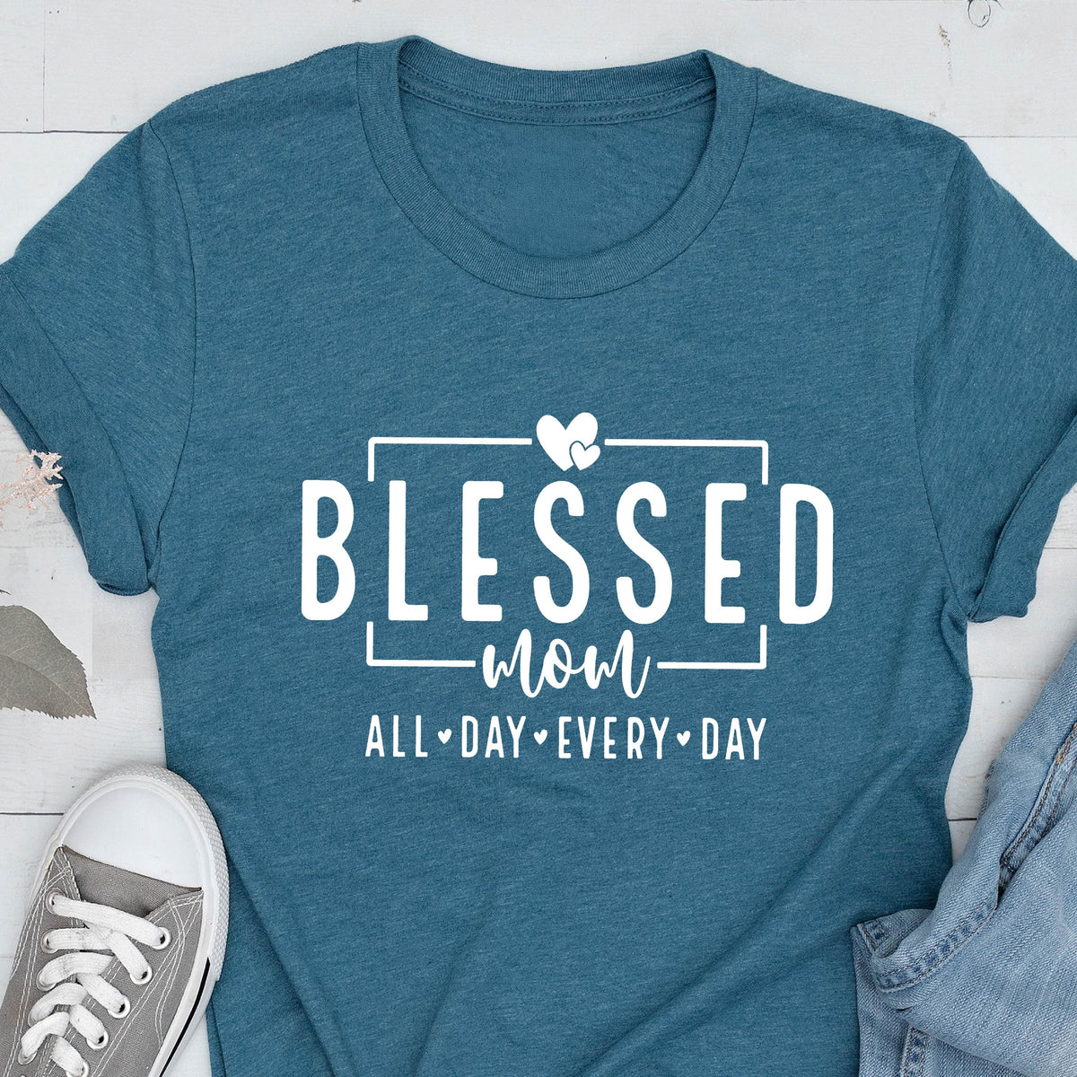 May include: Teal blue t-shirt with white text that reads "Blessed Mom All Day Every Day" with two white hearts above the word "Mom".
