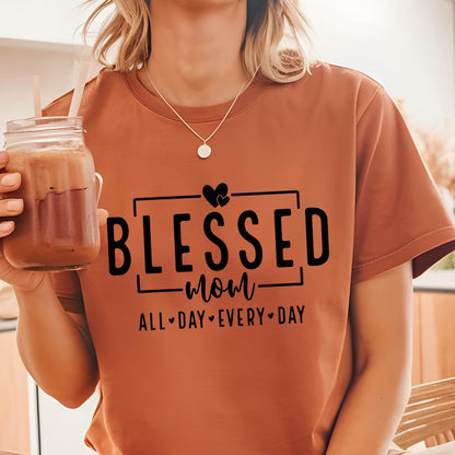May include: A brown t-shirt with the text "Blessed Mom All Day Every Day" in black lettering. Two small hearts are above the word "Blessed".