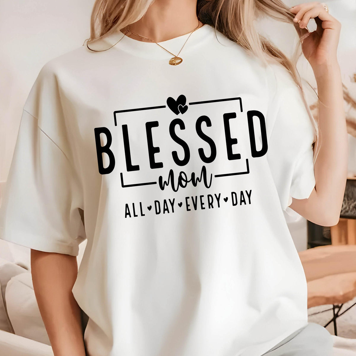 May include: White t-shirt with black text that reads "Blessed mom all day every day" with two hearts above the word "blessed".