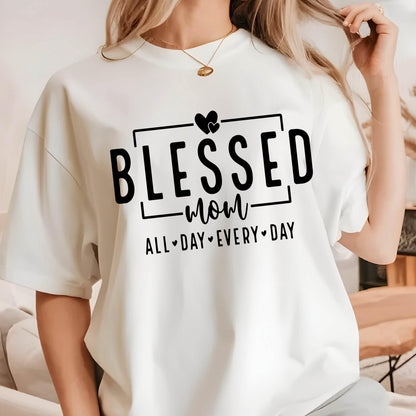 May include: White t-shirt with black text that reads "Blessed mom all day every day" with two hearts above the word "blessed".