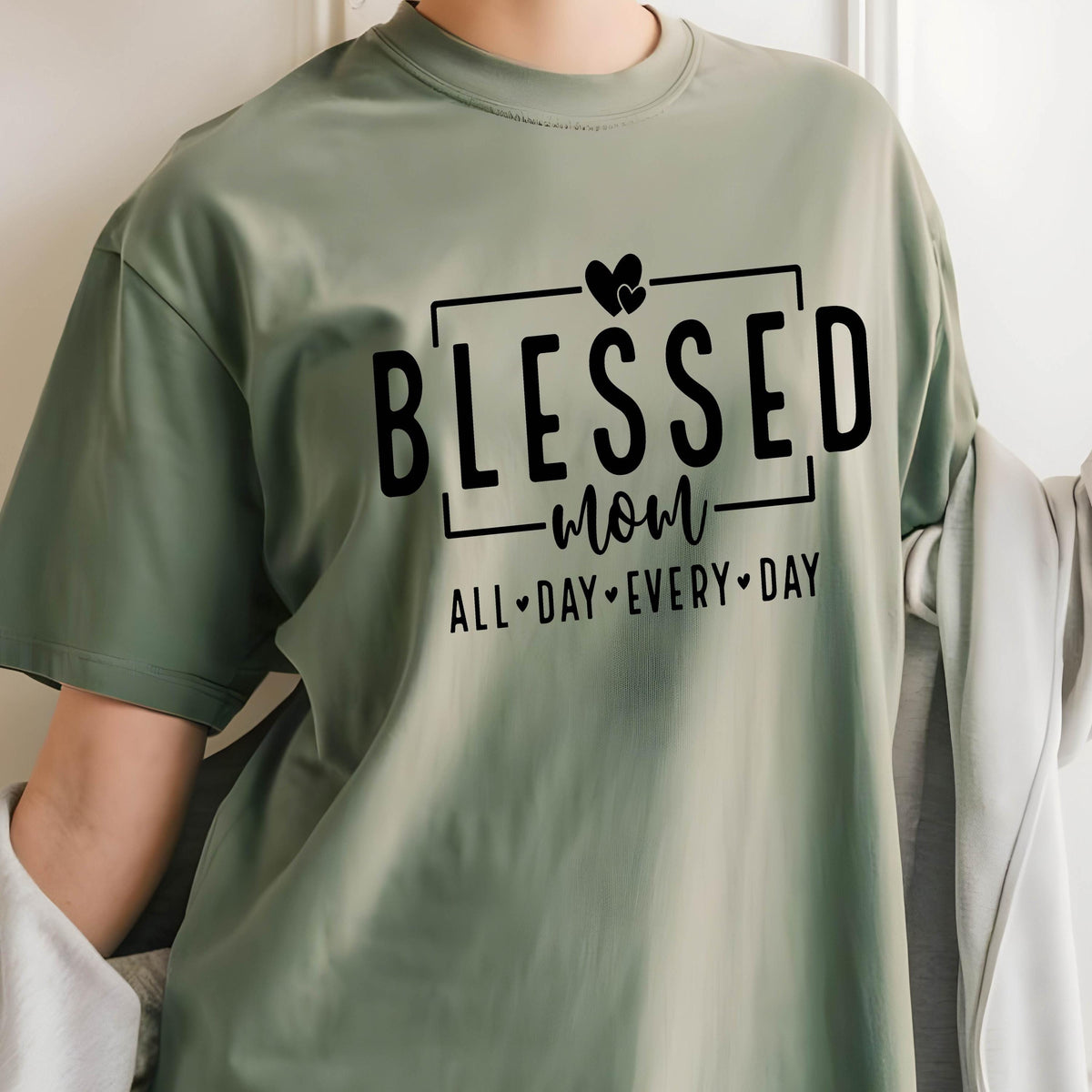 May include: A green t-shirt with the text "Blessed mom all-day every-day" in black lettering. The text is framed by a black rectangle and includes a heart symbol.