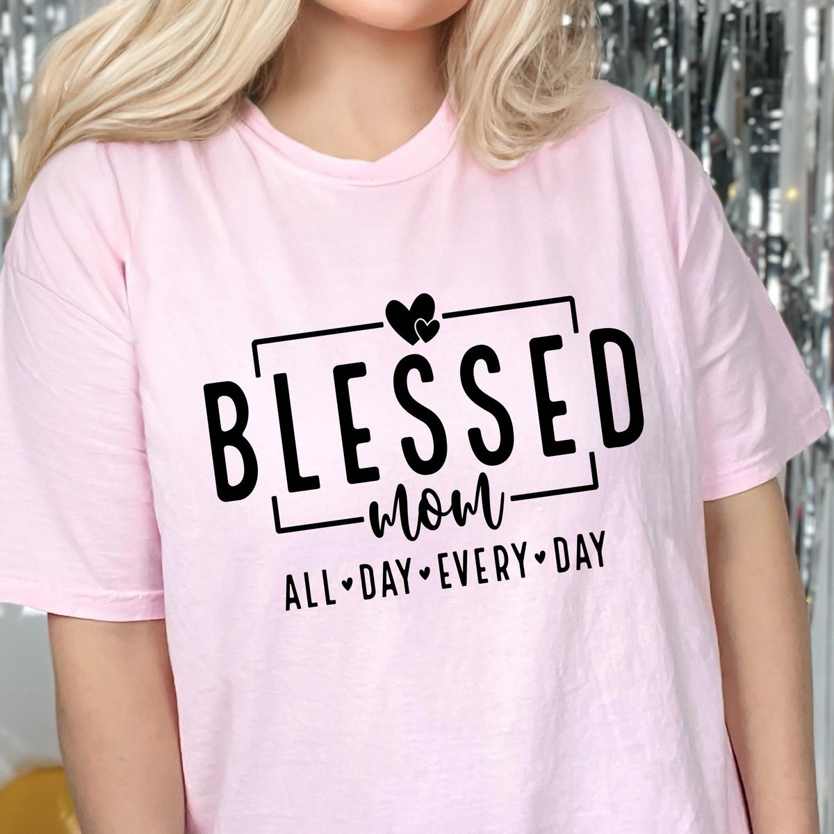 May include: Pink t-shirt with a black graphic that says "Blessed Mom All Day Every Day" with a heart symbol between each word.